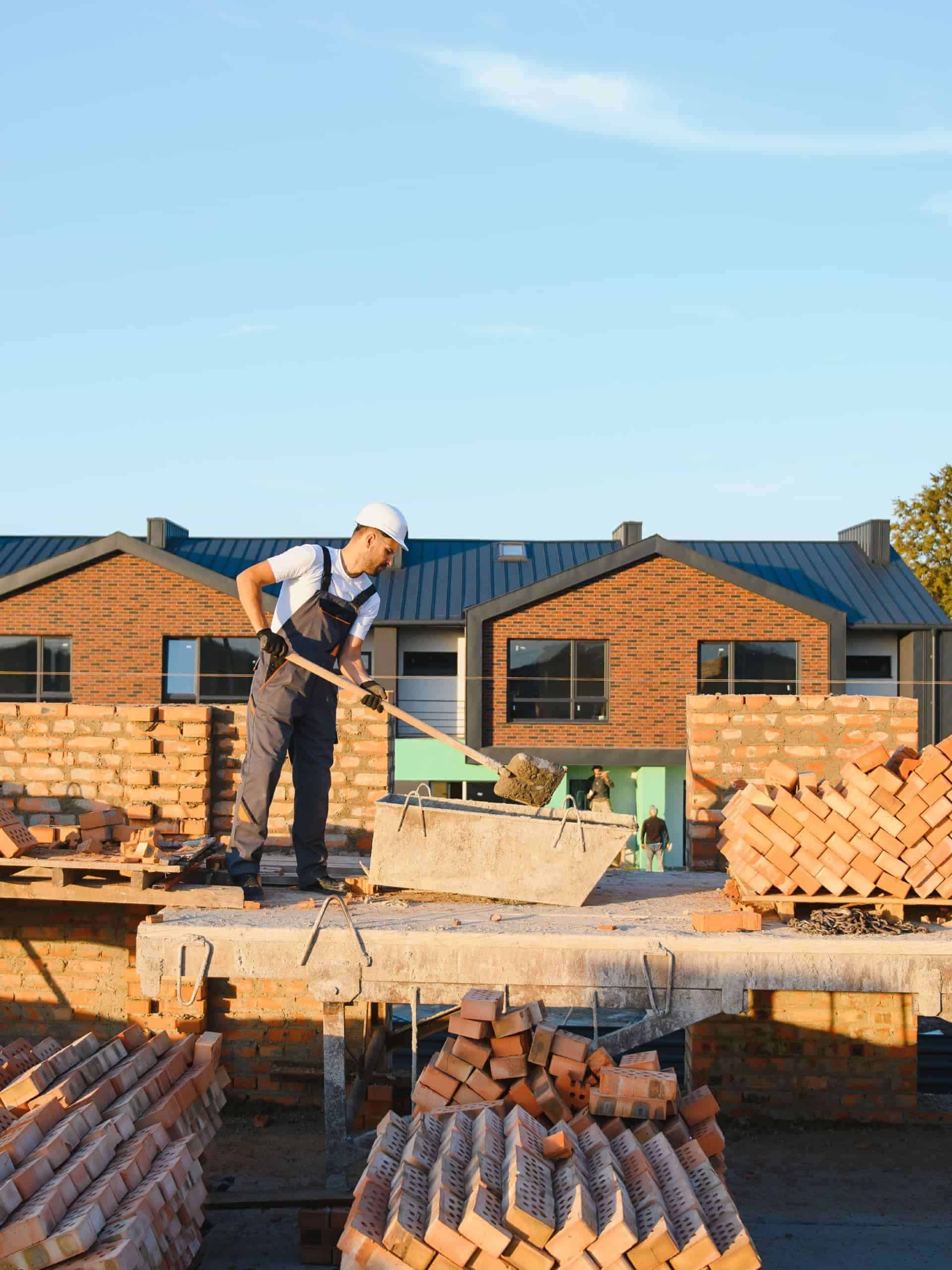 Construction foreman inspecting blueprints in front of a partially built modern home with scaffolding at sunset