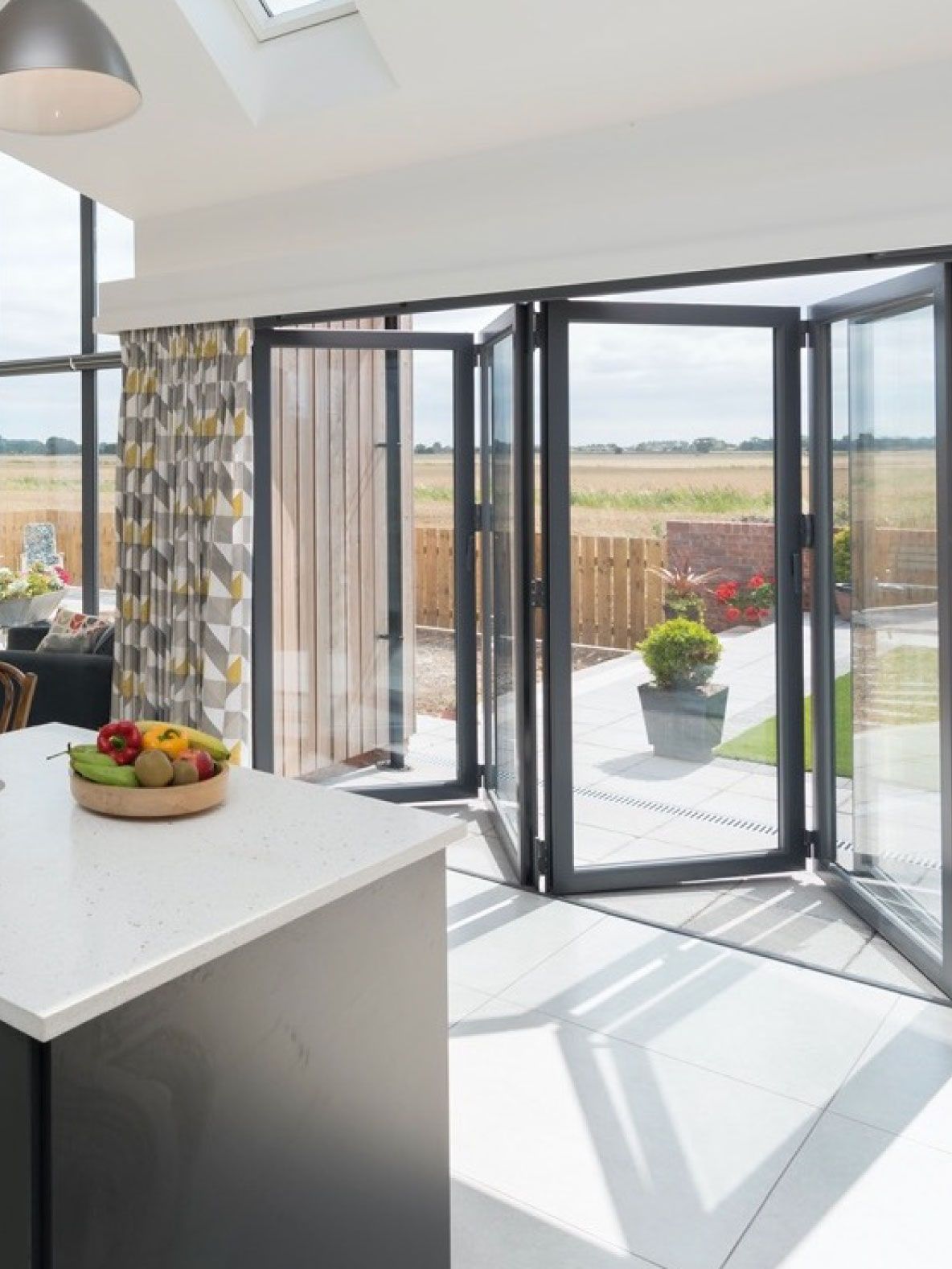 Bright modern kitchen extension with vaulted ceiling, triangular gable window and bifold doors opening to a landscaped garden